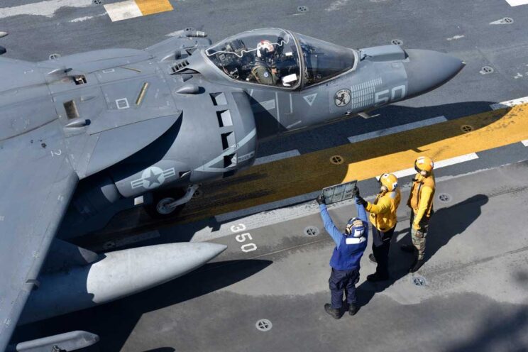 AV-8B+ z VMA-223 na okręcie desantowym USS Bataan (LHD-5); Atlantyk, 15 września 2016 r. Przed startem pilot otrzymuje ostatnie informacje dotyczące m.in. obciążenia samolotu, kąta ustawienia dyszy kierunkowych silnika oraz stanu nawierzchni pokładu. Pod owiewką widać oznaczenia misji bojowych.